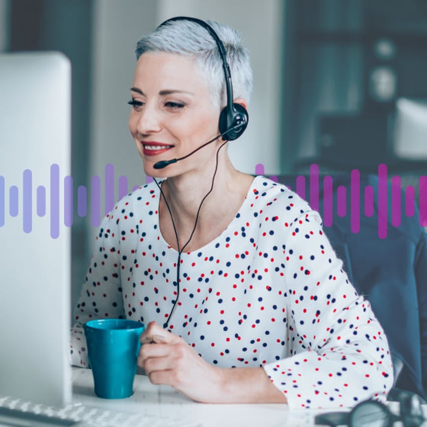 Photo of smiling female contact center agent looking at her computer screen as talks to a customer through her headset.